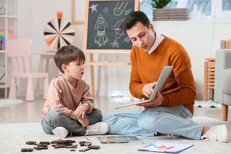 Man sits on ground and shows laptop to boy