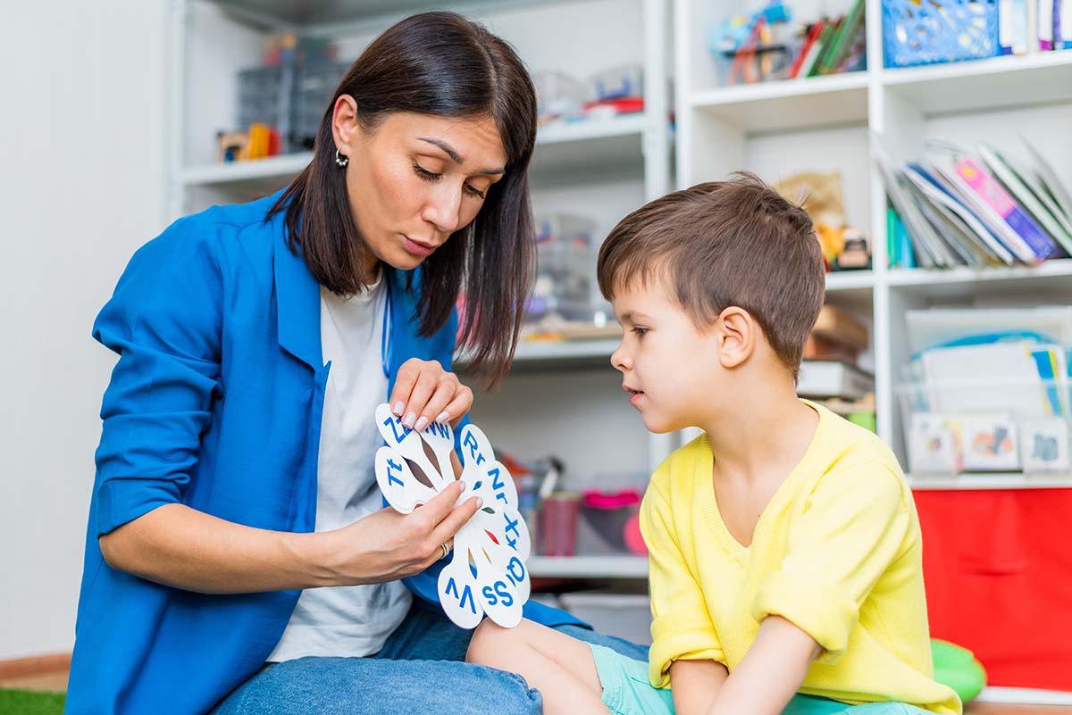 Woman shows child with autism letters during speech therapy