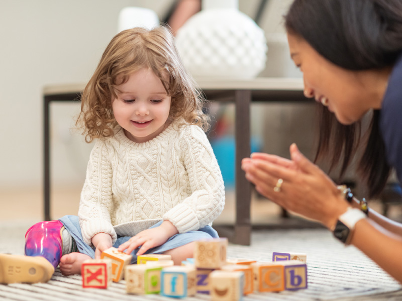 Therapist applauding young girl using toy blocks