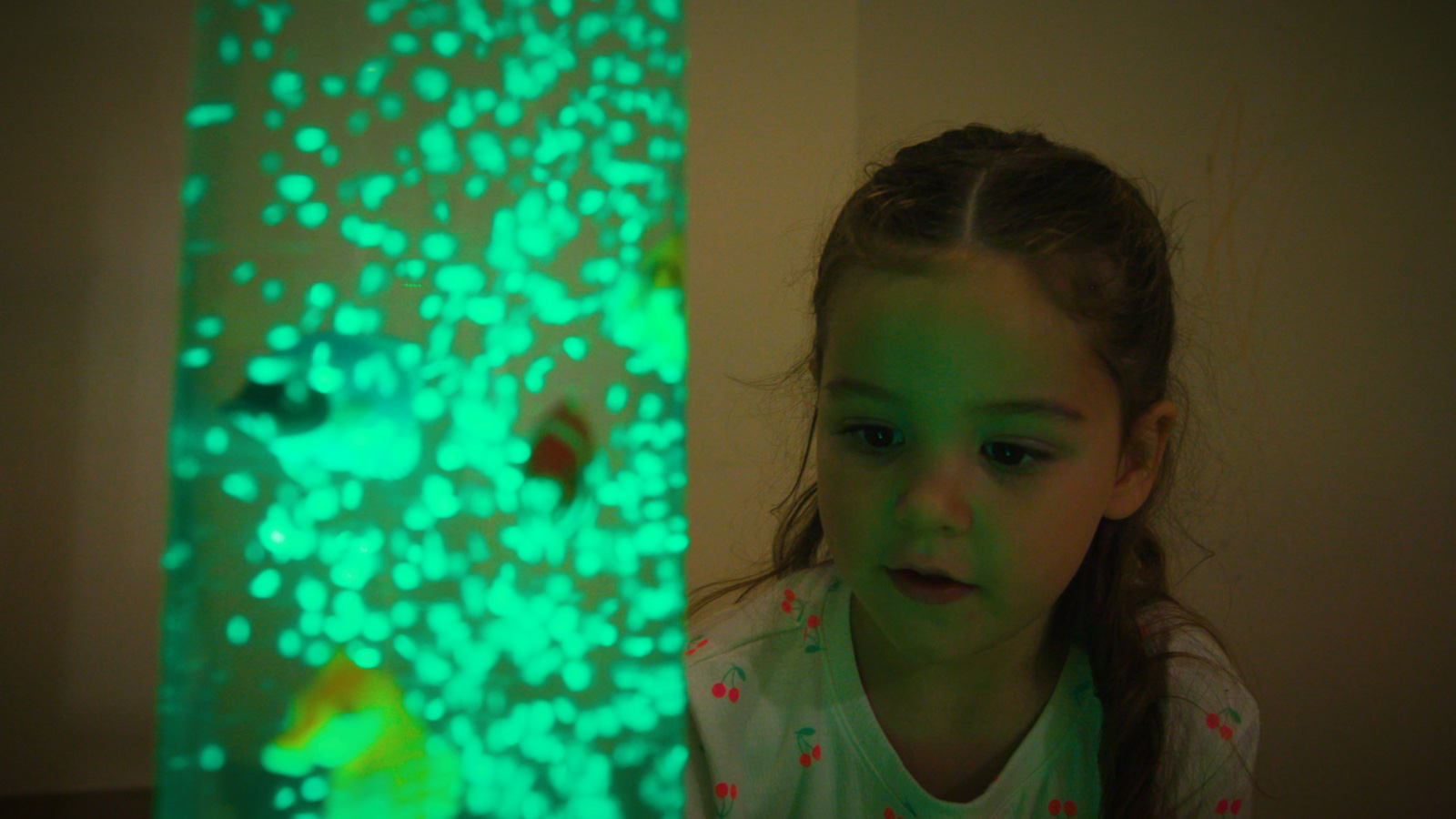 Child looking curiously at a bubble tube light with toy fish.