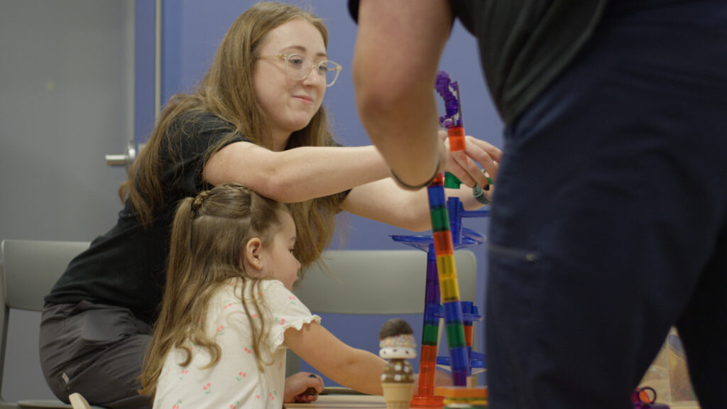 Adults building a tower using translucent blocks to play with a child.
