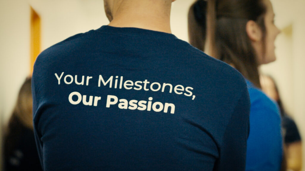 Person turn away from the camera with the phrase 'Your Milestones, Our Passion' on the back of their shirt.