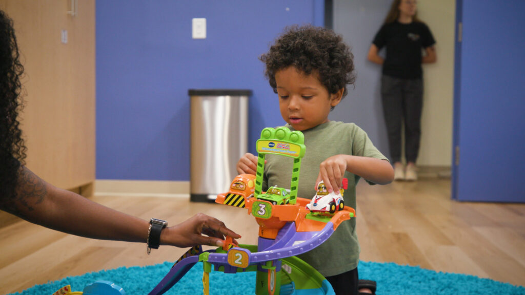 Child playing cars with a supervising adult.