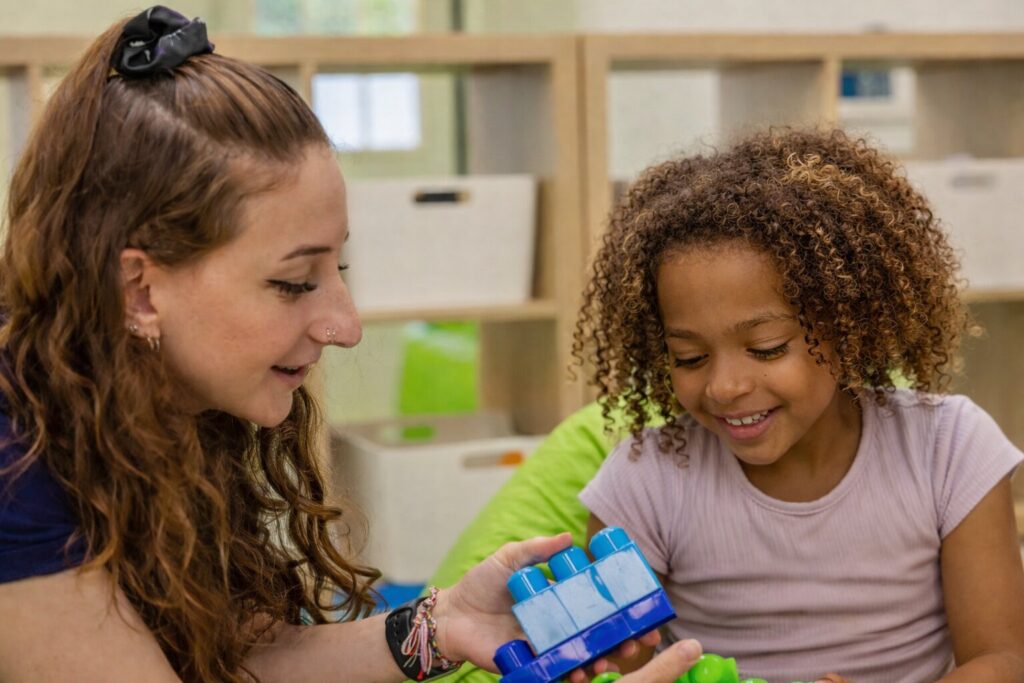 ABA therapist and child engaging in play-based therapy with building blocks.