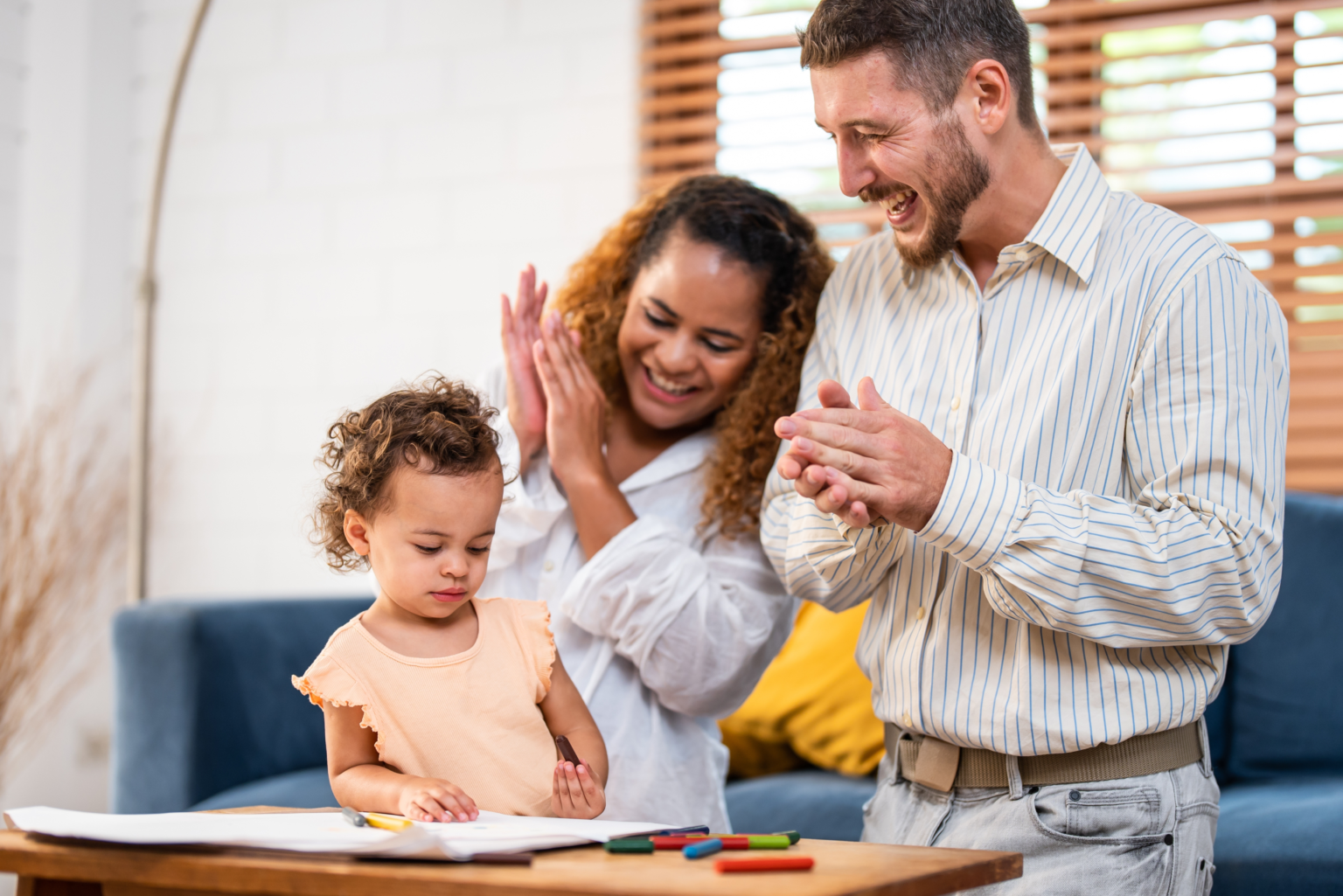 A young child drawing at a table while parents clap and encourage smooth activity transitions at home.