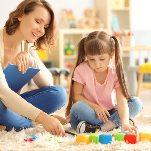 Female psychologist with cute little girl during play therapy